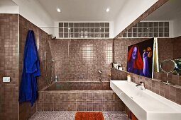 Modern designer bathroom with continuous mosaic tiling and transom window of glass bricks