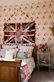 Wooden sleigh bed against floral wallpaper below Union Flag hanging on wall in traditional bedroom