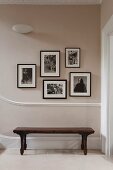 An old wooden bench in a hallway underneath framed black and white photographic prints