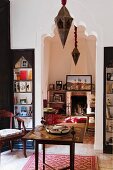 Arabian-style living area with glass display cabinets flanking arched open doorway leading to room with fireplace; ornate, Oriental, metal pendant lamps complement both rooms