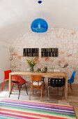 A collection of 20th century designer chairs at a wooden dining table in a kitchen with a transparent, blue hanging lamp and a striped rug