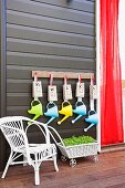 White rattan chair and retro style flower wagon cart in front of a black wall with colorful watering cans hanging on wall hooks