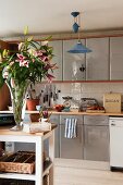 Fitted kitchen cupboards with various kitchen appliances on worksurface behind splendid bouquet of lilies on white-painted, narrow table