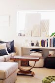 Books on shelf above beanbags and below home-made canvases on windowsill; corner sofa and coffee table in small living room