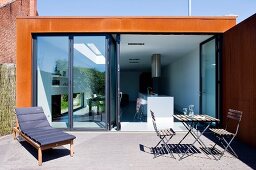 Terrace with lounger, table and chairs and a view through open folding doors into the kitchen