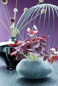 Gray felt vase with red clover in front of a ceramic vase with allium