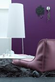 Contemporary designer couch next to white coffee table and minimalist standard lamp against purple wall