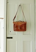 Vintage leather bag hanging from coat hook on white panelled door