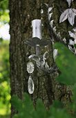Cast metal, floral candlestick decorated with crystal pendants hanging on tree trunk in garden