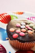 A cupcake decorated with chocolate glaze and colourful chocolate beans