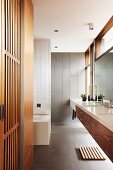 Designer bathroom - floating washstand with white top and fitted cupboard with slatted wooden door in grey-tiled bathroom