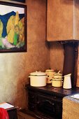 Angeschlagene Emailletöpfe auf altem Eisenherd in einer Küchenecke; gerahmtes Gemälde vor antik marmorierter Wandgestaltung