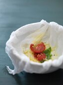 Leftover tomatoes, basil and olive oil in a bowl lined with a muslin cloth