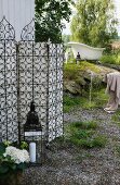 Garten mit schmiedeeisernem Paravent an Holzwand; im Hintergrund eine antike, freistehende Badewanne