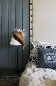 Relaxation area with fur rug and cushions in front of wooden wall with white fabric upholstery next to bedside lamp with animal-skin lampshade