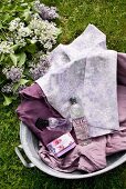 Blick auf rustikale Zinkwanne mit violetten Textilien, duftendem Seifenstück, Parfum und Duschgel