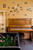 Foosball across from a piano along a wall with patterned wallpaper