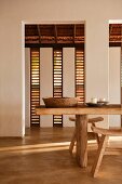Essbereich mit Lamellenfenstern und rustikalem Esstisch mit Hockern; auf dem Tisch eine einfache Holzschüssel