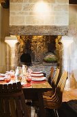 Wooden chairs at set table in front of open fireplace with columns in rustic atmosphere