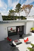 Blick auf grosse Terrasse eines modernen Wohnhauses mit verschiedenfarbigen Butterfly Sesseln und Frau in offener Terrassentür