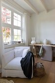 White upholstered armchair in front of writing desk by the window