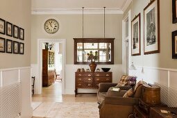 Antique wooden drawers and mirror in hallway with leather armchairs and vintage trunks