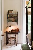Art deco gooseneck desk lamp on small wooden reading table in bedroom with four poster bed and footstool
