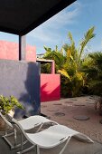 Modern sun loungers on terrace looking out to courtyard with round paving stones and palm plants