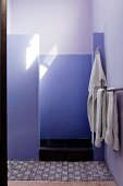 Stone shower cubicle painted in a lilac hue with black and white mexican floor mat