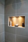 Bathroom with gray wall tiles and bath accessories in an illuminated wall niche