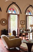 Indian residential house - upholstered armchair on red tiled floor in elegant living room with open terrace doors and coloured fanlights in pointed arches above