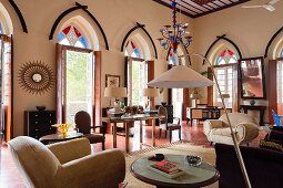 Indisches Wohnhaus - Elegantes Wohnzimmer mit moderner Stehlampe im Loungebereich und offene Terrassentüren mit farbigen Oberlichtern in Spitzbogenform