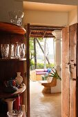 Glasses on corner shelving next to open door with view into interior of Indian house and of garden beyond