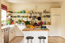 Fröhliche Küche mit farbenfrohem Geschirr auf langem Küchenregal; in der Mitte die Kücheninsel mit einer Arbeitsplatte aus hellem Massivholz