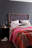 Artistic atmosphere in modern bedroom - bed with headboard made from colourful cords against black-painted wall