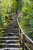 Traditional stone stairs on a slope with a wooden hand railing on one side in a Japanese garden in Portland