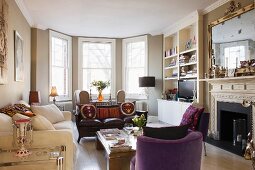 Englisches gemütliches Wohnzimmer mit Erkerfenstern davor Sitzgruppe und offener Kamin mit Polstermöbeln und Couchtisch