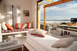 Living room and terrace with an ocean view - cozy upholstered day beds by an open picture window in front of a terrace