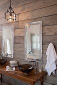 Dark, wash basin on a wooden table with designer fittings and mirrors on a rustic, wood plank wall