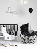 White Bauhaus rocking chair and black, vintage-style pram next to cot with bars painted black and white
