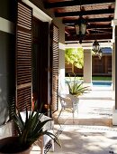 Elegant house with wooden door shutters and encircling porch on pillars in front of pool in garden