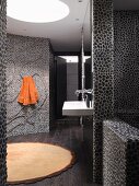 Designer bathroom with floor-to-ceiling, dark pebble mosaic tiled walls and curved wall