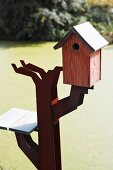 Small, red varnished nesting box on artistic metal support