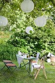 Set table with bench and rustic chairs below lanterns hanging from tree in garden
