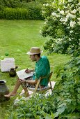 Man wearing summer clothing sitting on chair drawing in garden