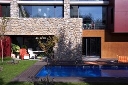 Swimming pool in garden of modern house with stone wall