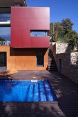 Modern building with brightly-coloured and glazed facade; swimming pool and wooden terrace in foreground