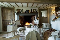 Nostalgic, country-house-style living room with vintage furniture and textiles in natural shades; fire burning in large, open fireplace in background