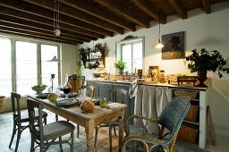 Simple kitchen counter with curtained front and storage baskets below small lattice window in cosy, country-house kitchen with rustic wooden table and vintage chairs