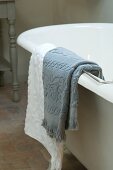 Grey and white towels hanging over edge of free-standing bathtub